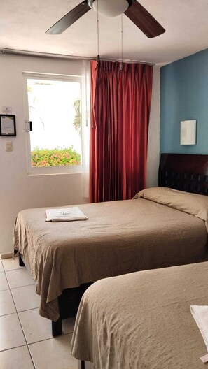 A room with two beds, a ceiling fan, a window with curtains, and a blue wall. - Hotel Avenida (Campeche)