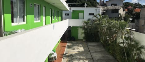 A green and white building with multiple windows, a tiled pathway, and some greenery.