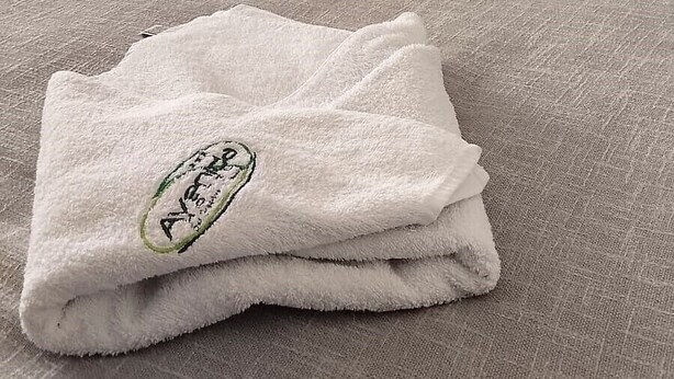 Un asciugamano piegato con un logo su un letto in una stanza con un armadio scuro e una ventola a soffitto.