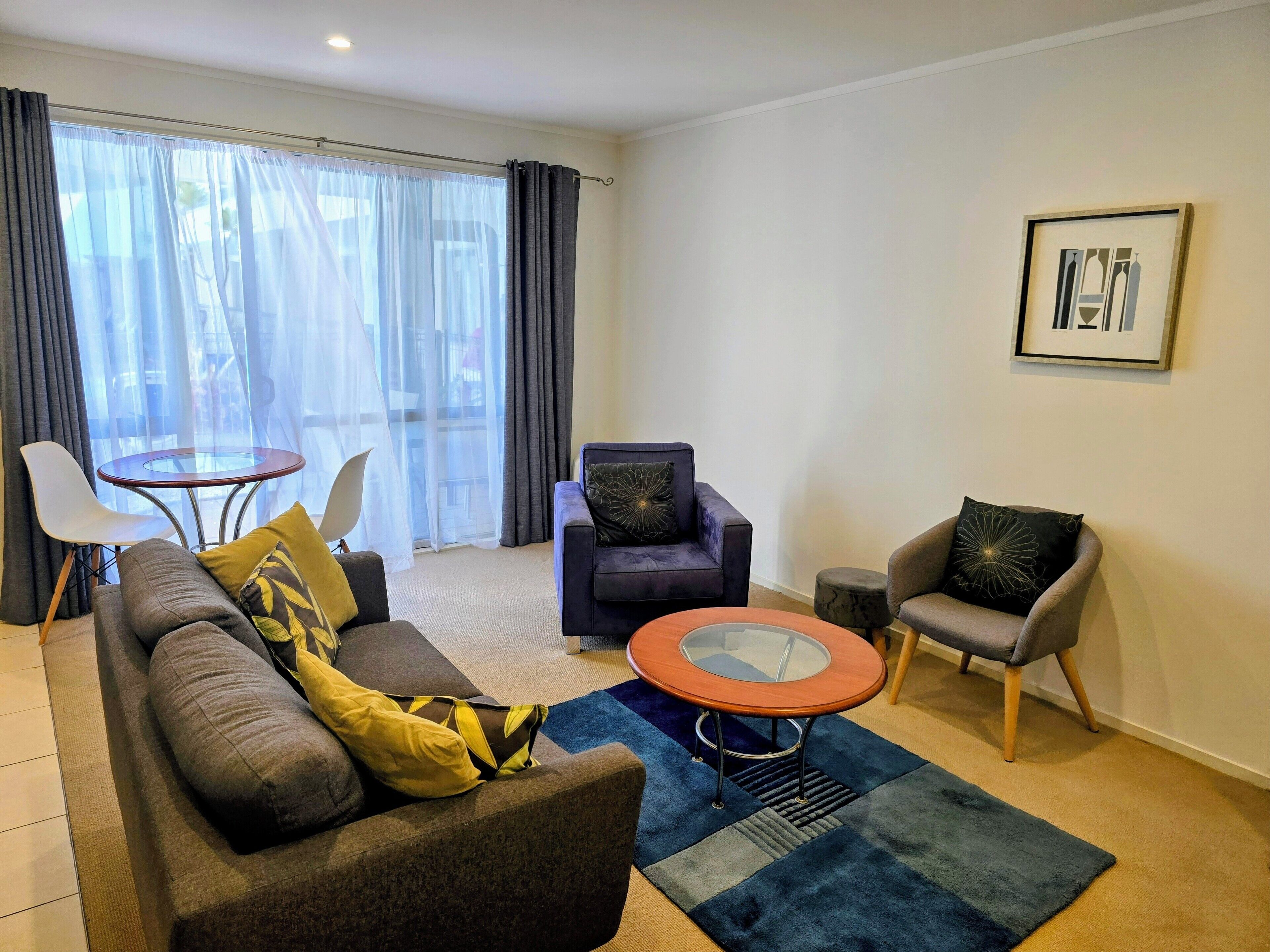Una sala de estar moderna con un sofá, dos sillones, una mesa de centro de vidrio y una pequeña mesa redonda.