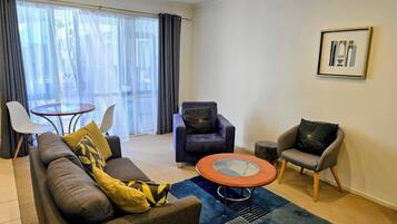 Una sala de estar moderna con un sofá, dos sillones, una mesa de centro de vidrio y una pequeña mesa redonda.