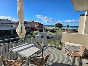 A balcony with a table and chairs, overlooking a residential area and a beach.