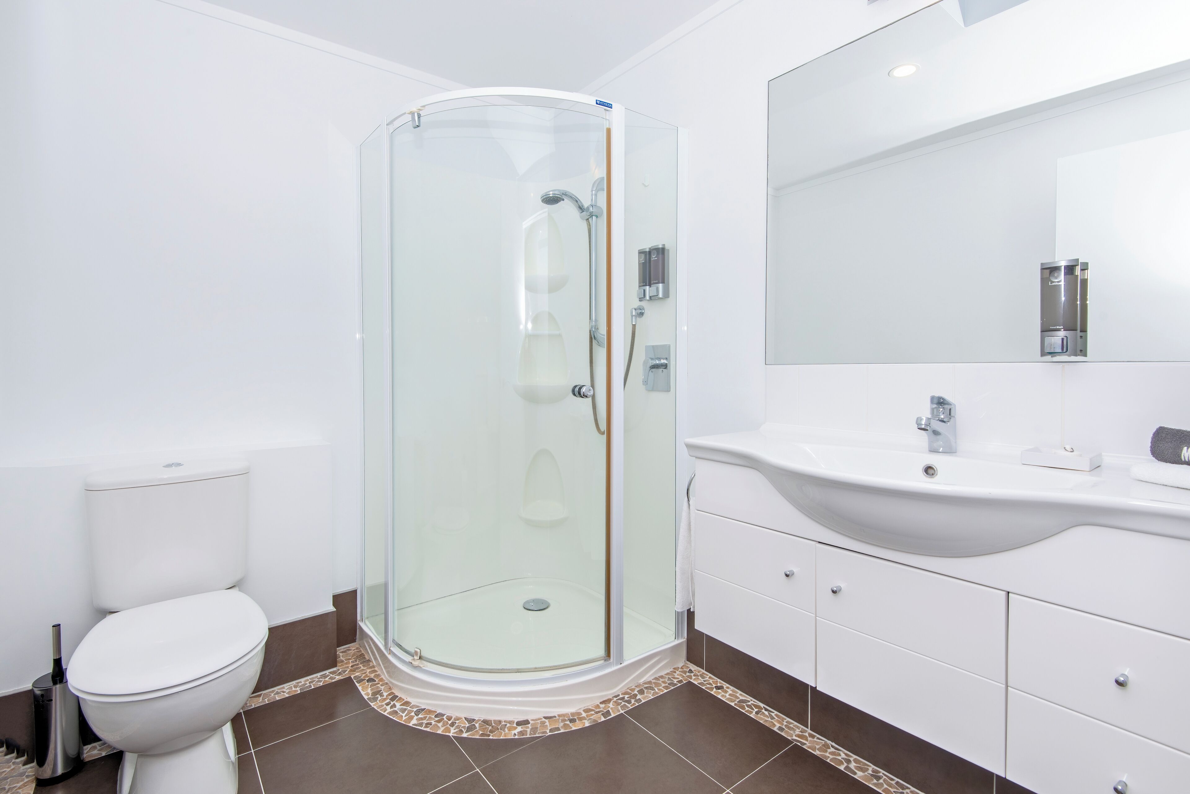 A modern bathroom with a glass-enclosed shower, a white toilet, and a white vanity with a large mirror.