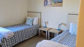 Een kamer met twee bedden, elk voorzien van een beddekleed met een patroon, een tafeltje met een lamp en een schilderij aan de muur.