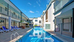 A swimming pool with lounge chairs, a clear sky, and modern buildings with balconies. - Beachpoint Apartments (Ohope)