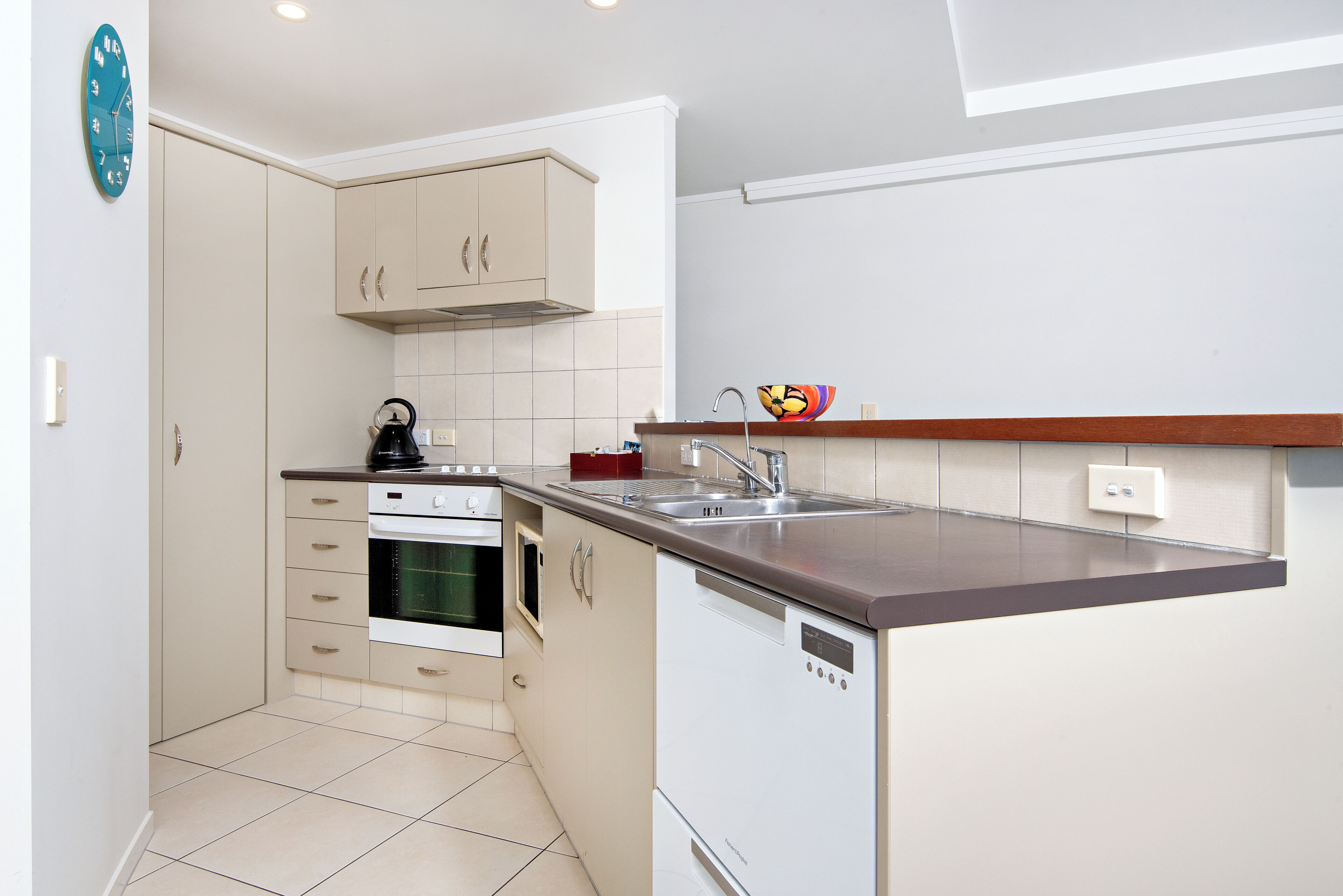 Una cocina compacta con armarios color beige, horno empotrado, lavavajillas y pileta de acero inoxidable.