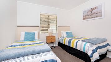 A bedroom with two beds, a nightstand, a window with blinds, and a framed picture on the wall.