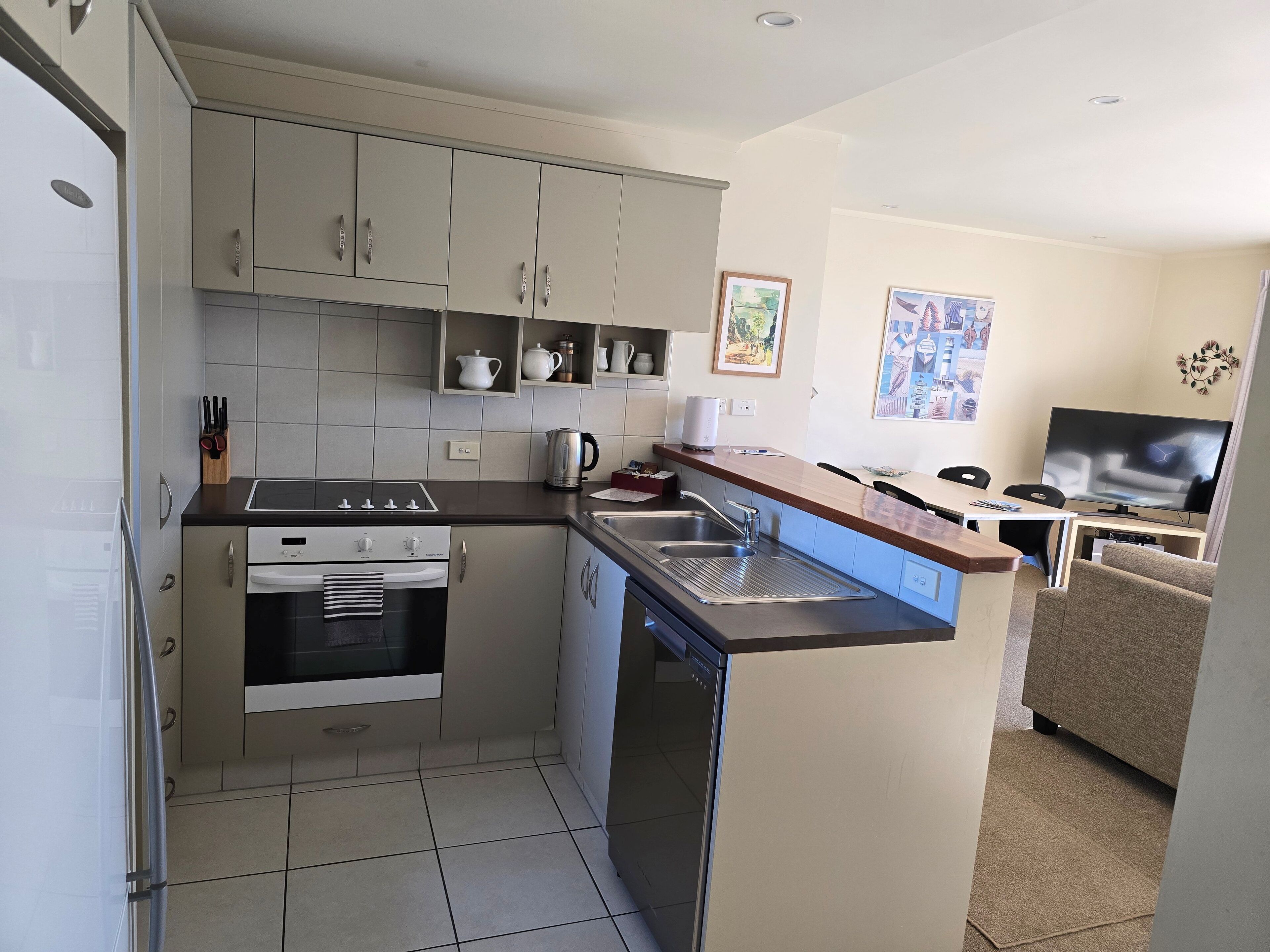 Een kleine keuken met een fornuis, oven en vaatwasser. Er is een zithoek met een televisie.