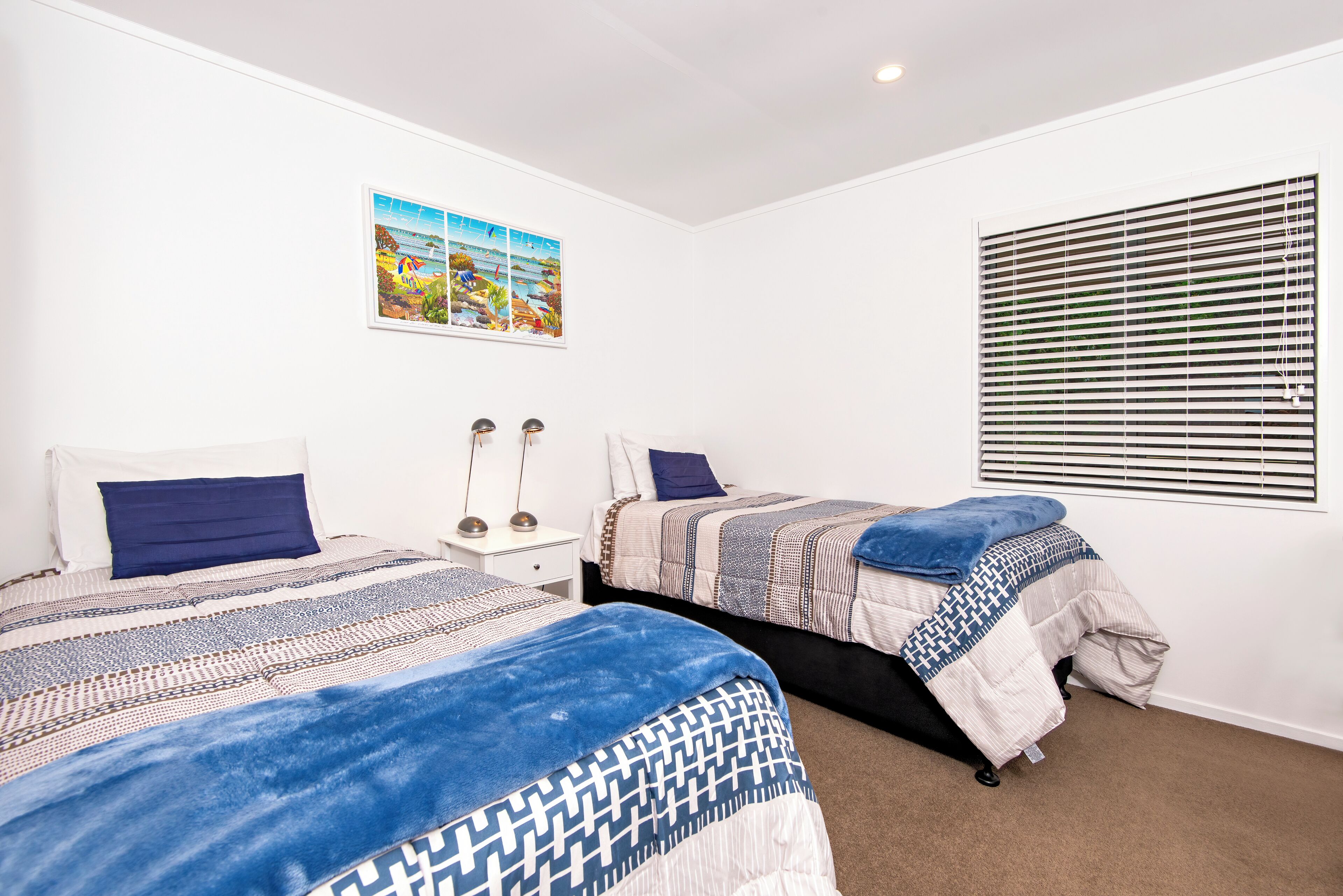 A bedroom with two beds, a nightstand, a wall-mounted picture, and a window with blinds.