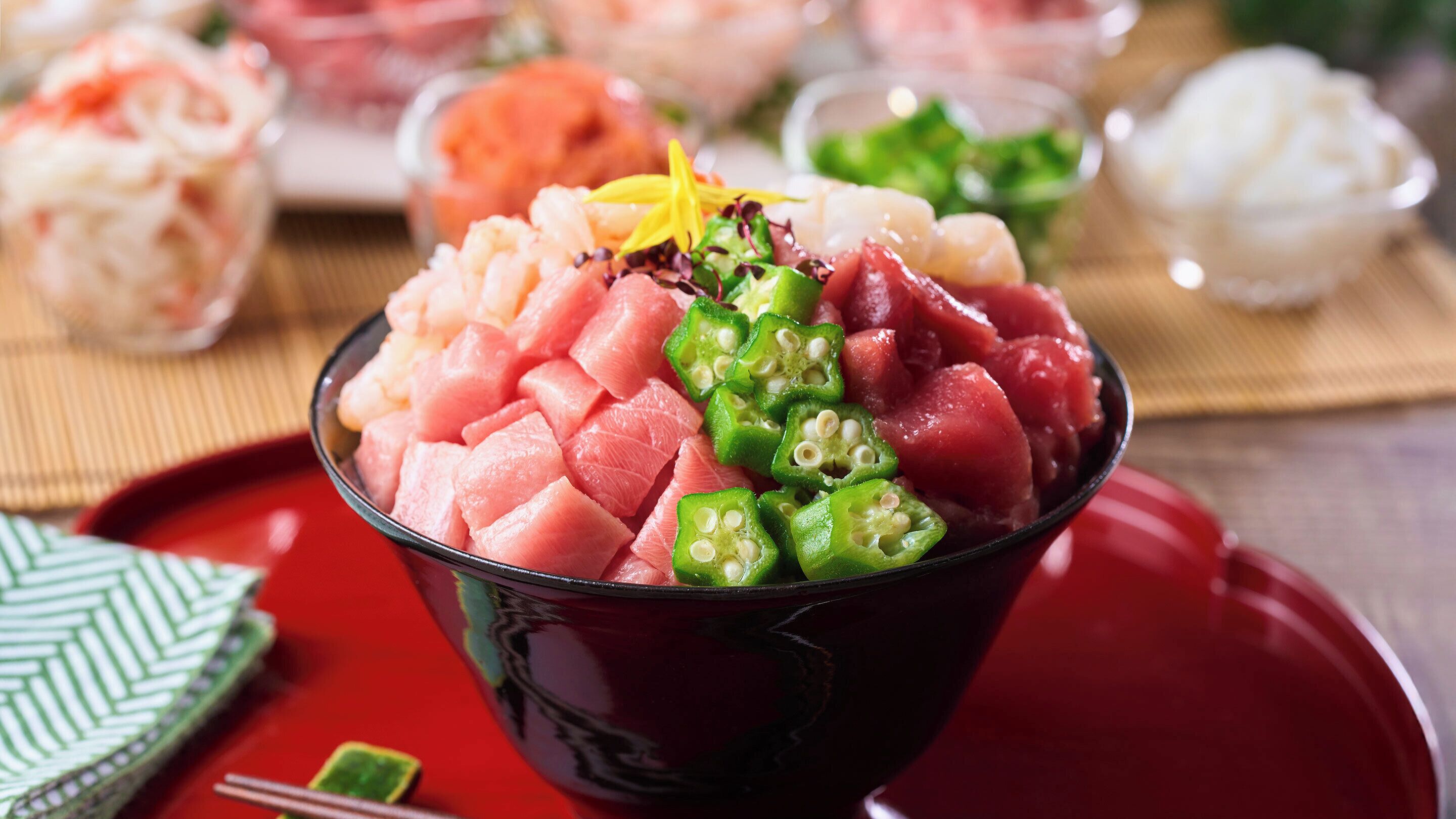 A bowl of sashimi with green vegetables on a red plate.