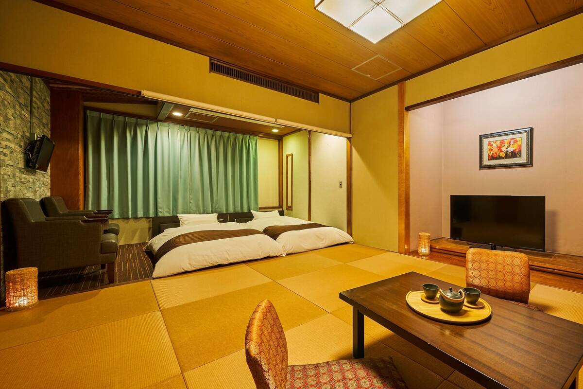 A traditional Japanese-style room with tatami flooring, a bed with a green curtain, a television, and a table with a tea set.