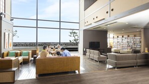 A spacious lobby with a large window, a seating area with sofas and chairs, a television, and a bookshelf.
