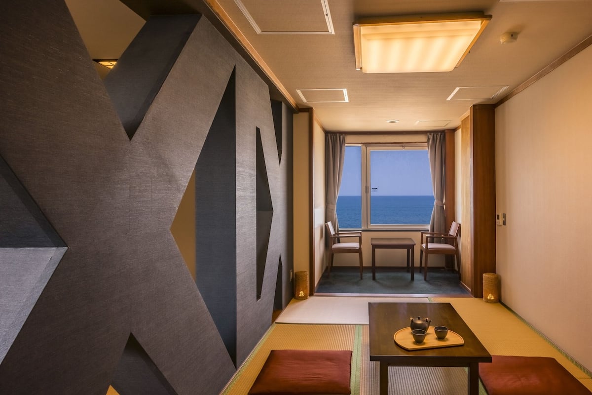 A room with a view of the sea, a table with a teapot and cups, and traditional Japanese tatami flooring.