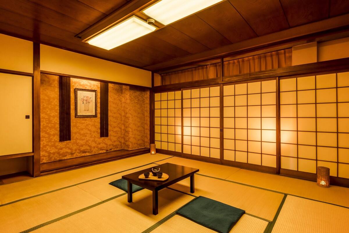A traditional Japanese room with tatami flooring, a low table with tea set, sliding doors, and a framed picture on the wall.