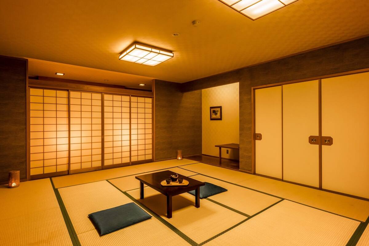 A traditional Japanese room with tatami flooring, sliding doors, a low table with tea set, and a small table with a vase.