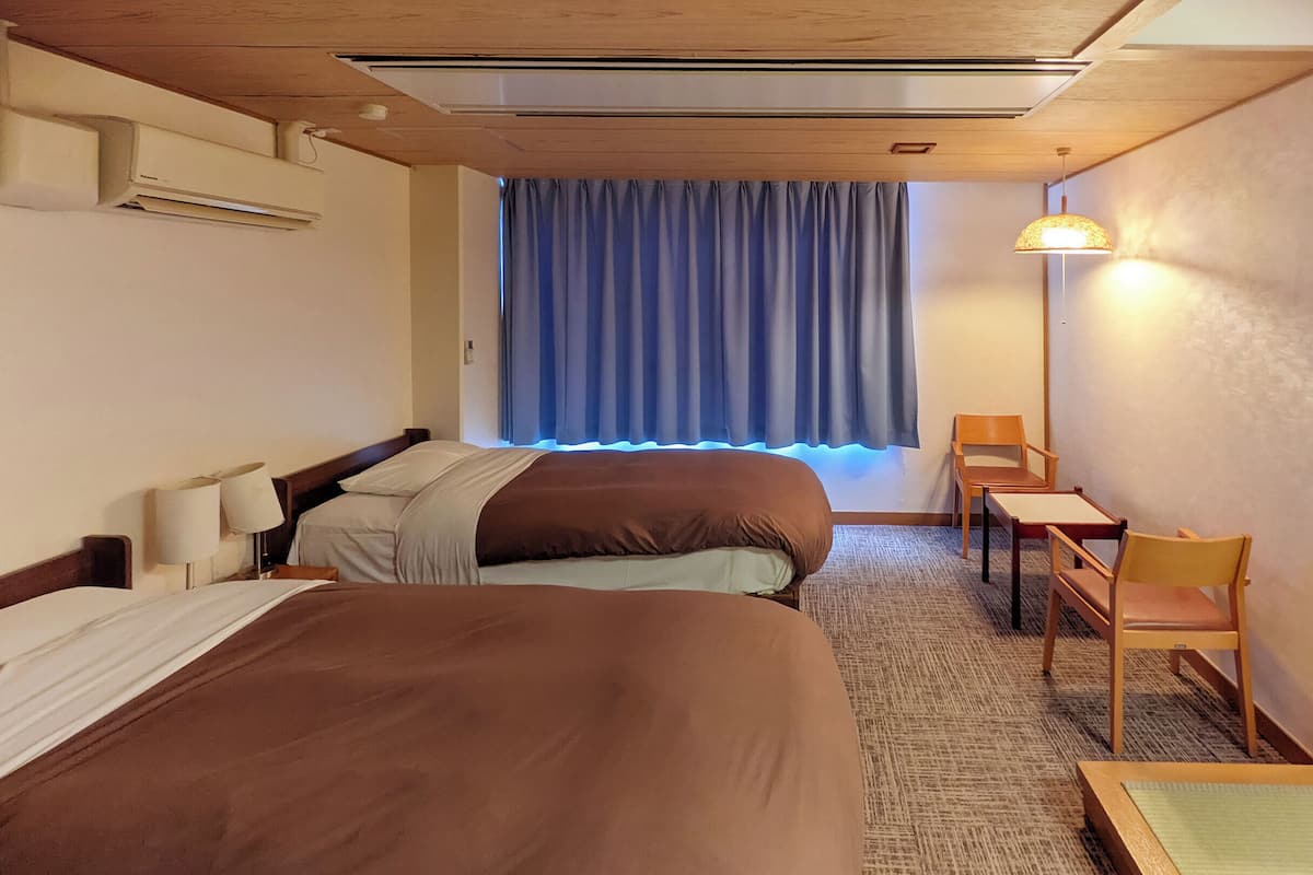 A hotel room with two beds, a desk, a chair, a lamp, and a window with curtains.