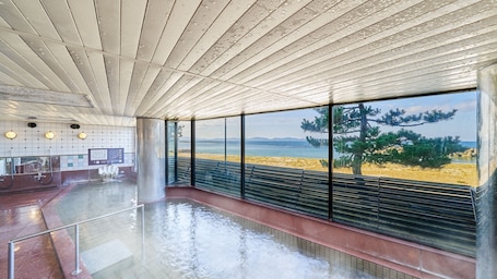 A spacious indoor area with a large window overlooking a beach, a tiled floor, and a ceiling with a unique design.