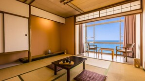 A traditional Japanese room with tatami flooring, a low table with tea set, and a view of the sea through large windows. - Ooedo Onsen Monogatari Kaike (Yonago)