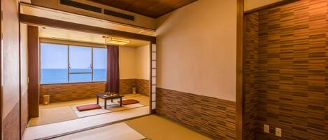Una habitación japonesa tradicional con suelo de tatami, una mesita con un juego de té y vistas al mar a través de un ventanal grande.