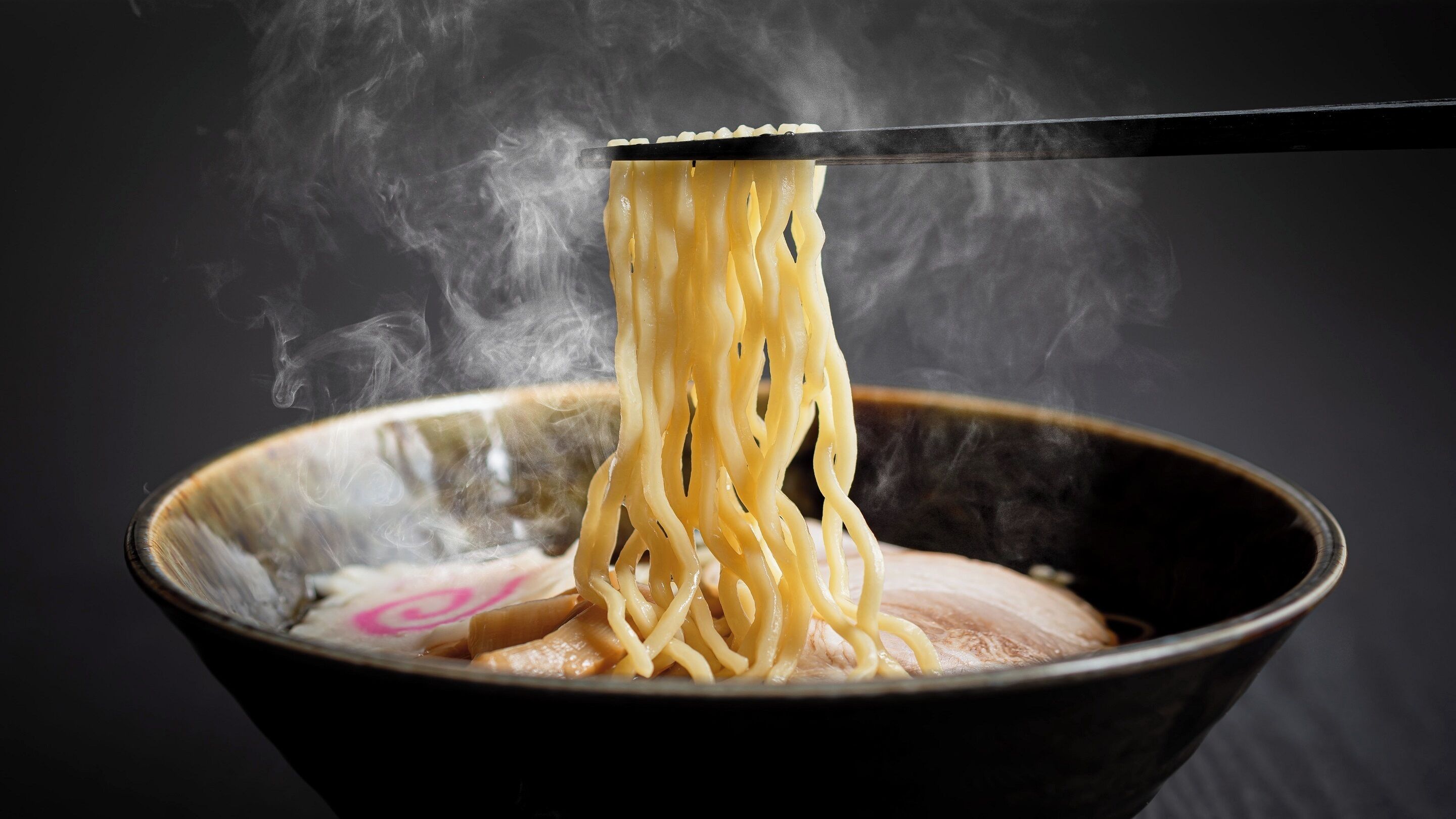Un bol de nouilles est soulevé à l’aide de baguettes, et de la vapeur s’en échappe.
