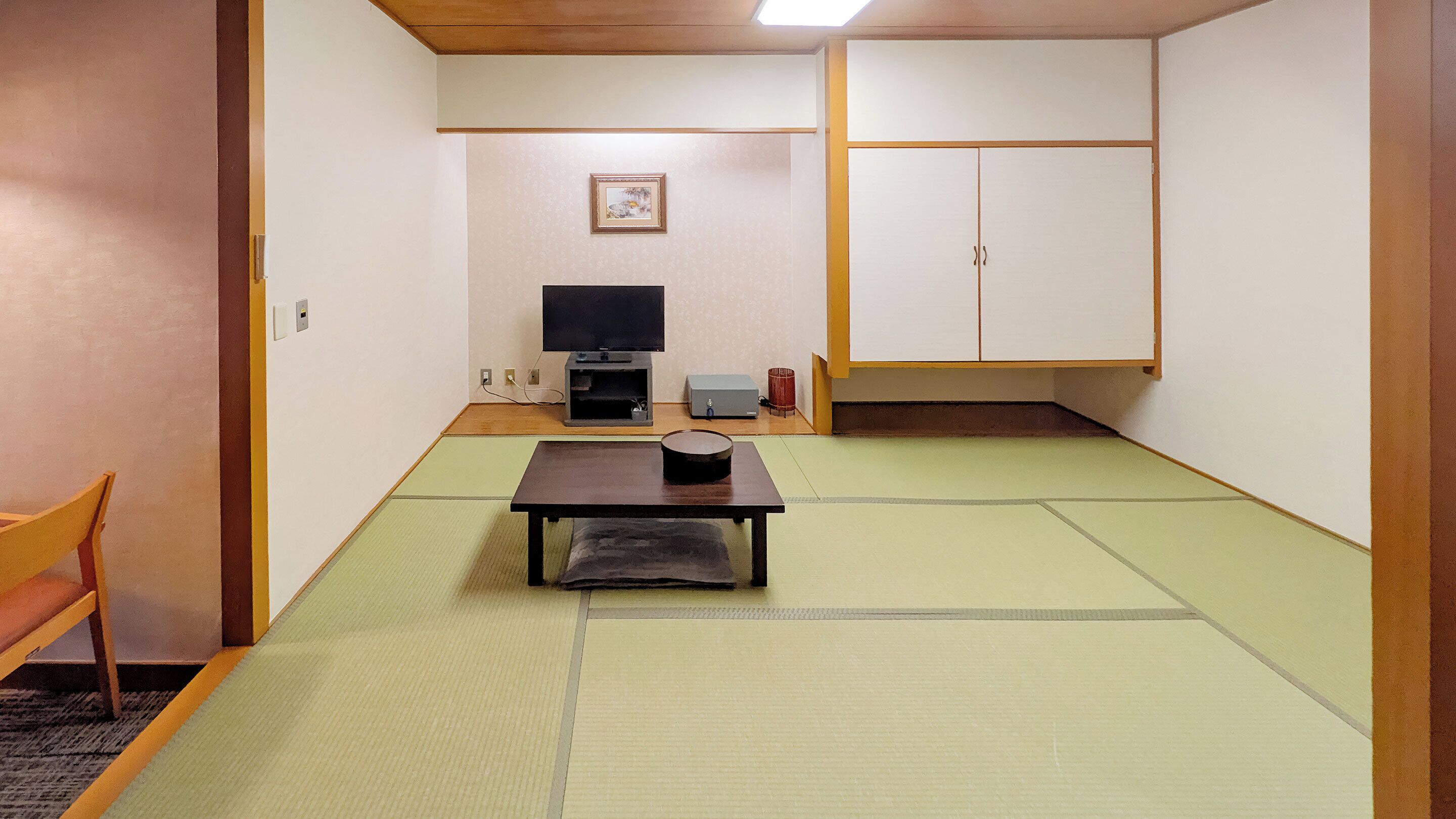 A traditional Japanese room with tatami flooring, a low table with a black container, a television, and a wardrobe.
