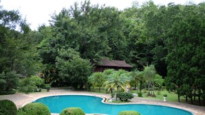 A swimming pool surrounded by lush greenery and a small building in the background. - Lanna Resort (Hang Dong)