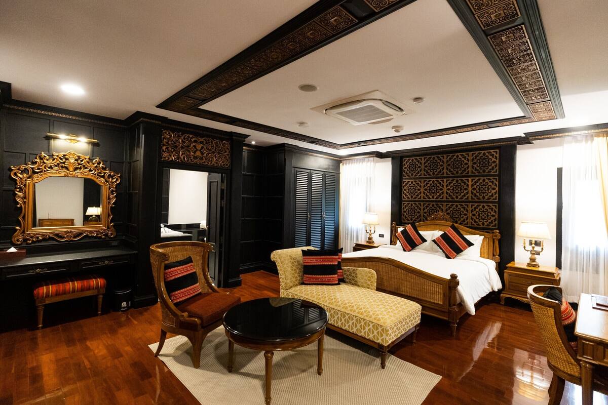 A spacious bedroom with a large bed, a sitting area with a chair, a desk, and a mirror.