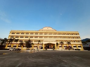 A multi-story building with a central entrance, palm trees, and a clear sky. - Ranong Garden Hotel (Ranong)