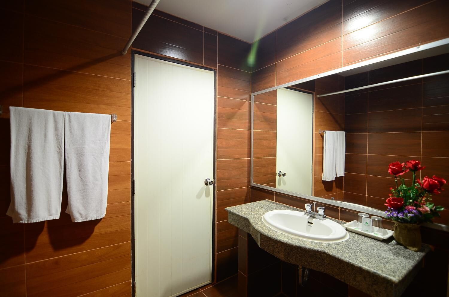 A bathroom with a wooden wall, a white door, a granite sink, and a mirror.