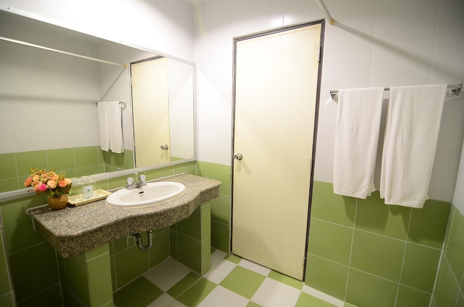 Un baño con lavamanos de granito, un espejo, un inodoro y paredes con azulejos blancos y verdes.