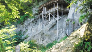 Une construction traditionnelle en bois, intégrée à une falaise et entourée d’une végétation luxuriante.