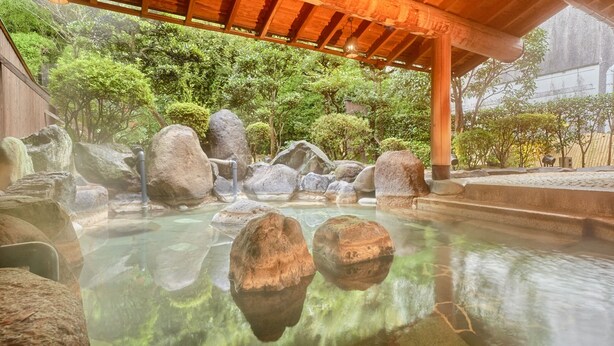 Un jardin japonais traditionnel avec un bassin en pierre, de gros rochers et une structure en bois située au-dessus.