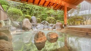 Un jardín japonés tradicional con un estanque de piedra, rocas grandes y una estructura de madera sobre él.