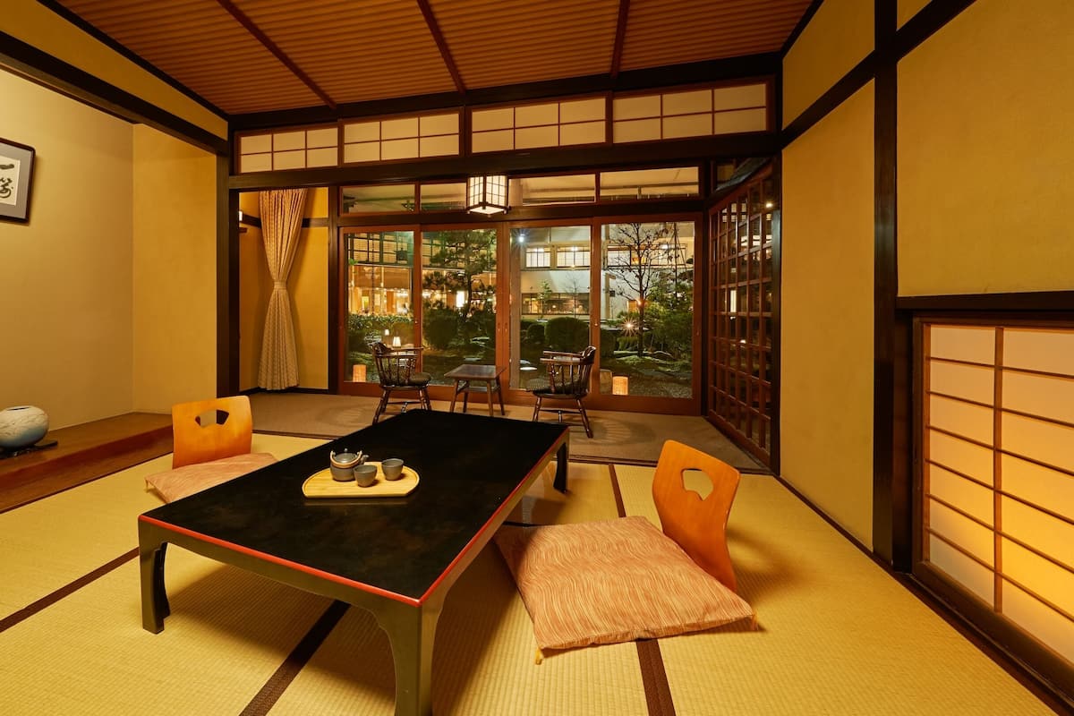A traditional Japanese room with tatami flooring, a low table with a tea set, and sliding doors leading to a garden.