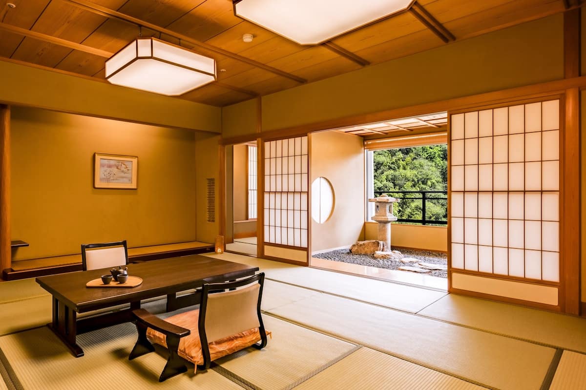 A traditional Japanese room with tatami flooring, a low table with a cushion, a wooden chair, and a sliding door leading to a garden.