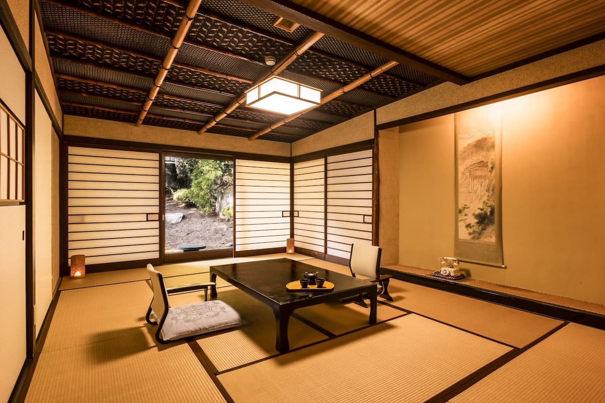 A traditional Japanese room with tatami flooring, a low table with a cushion, and sliding doors.