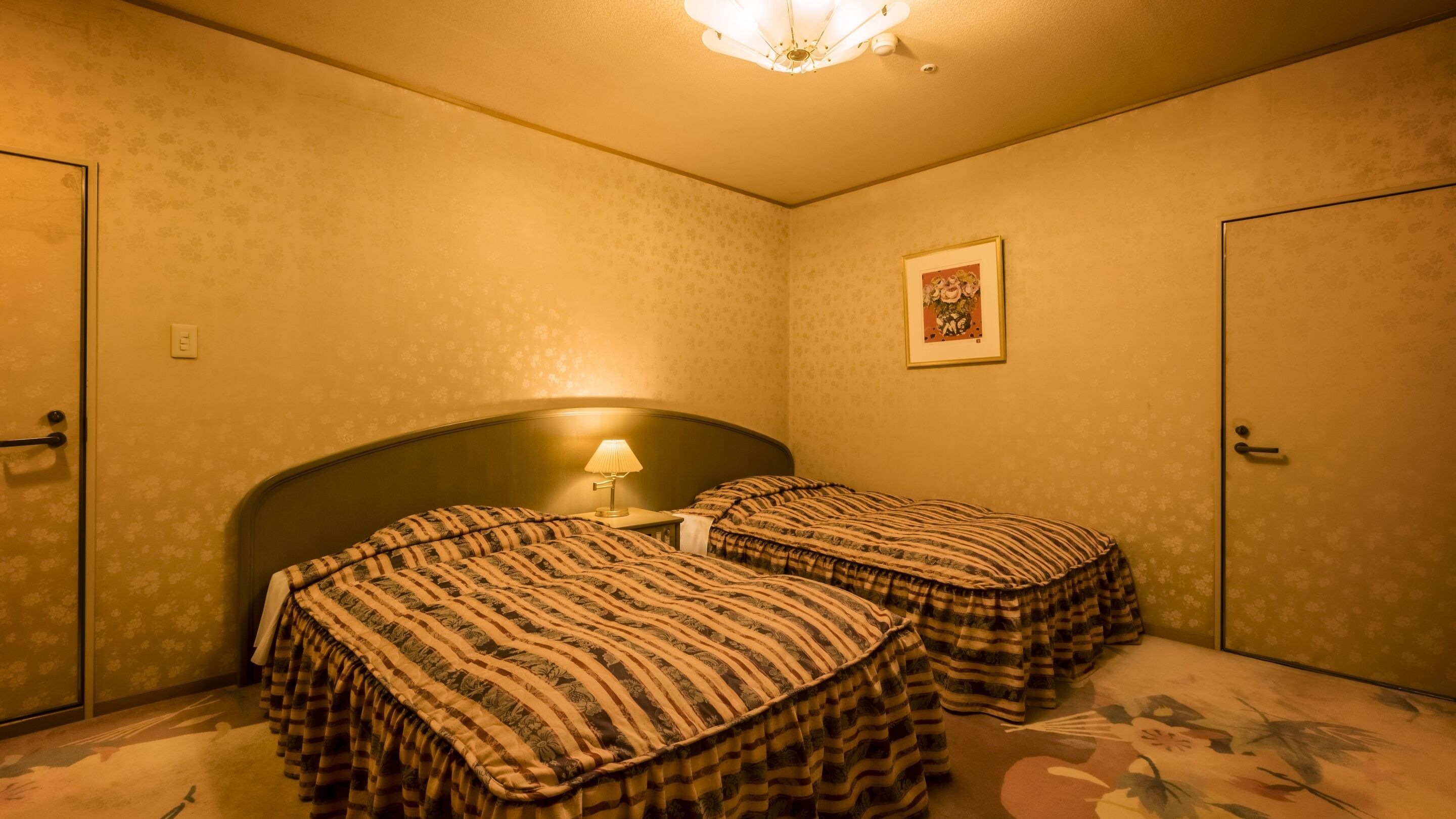 A room with two beds, a nightstand, a lamp, a framed picture on the wall, and a door.