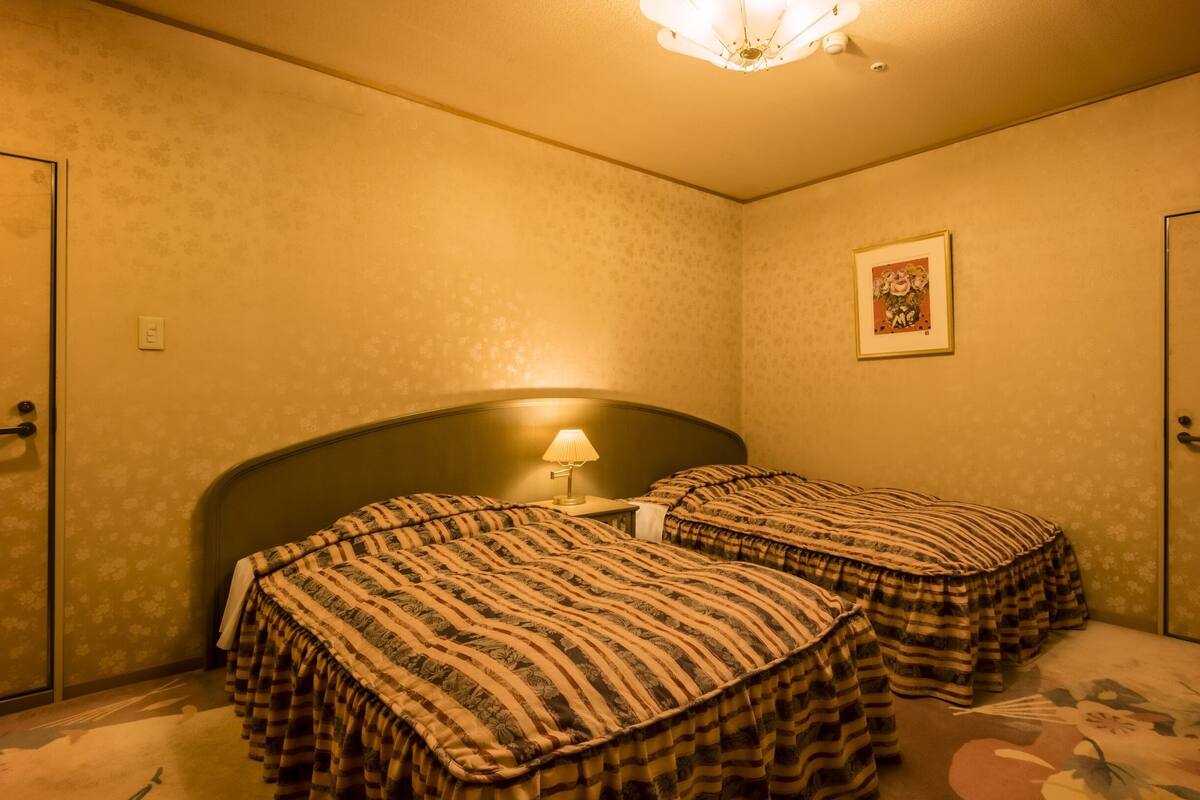 A room with two beds, a nightstand, a lamp, a framed picture on the wall, and a door.