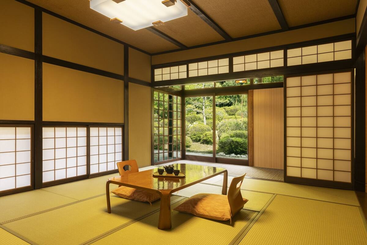 A traditional Japanese room with tatami flooring, a low table with cushions, and sliding doors with a view of a garden.