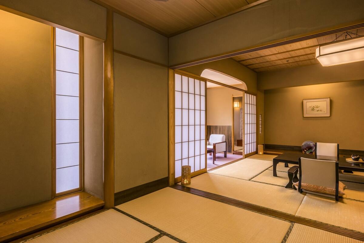 A traditional Japanese room with tatami flooring, a low table with a cushion, and sliding doors.