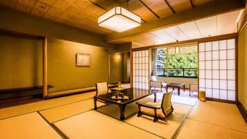 Una habitación tradicional japonesa con suelo de tatami, una mesa baja con juego de té y puertas correderas que dan a un balcón con vistas a árboles.