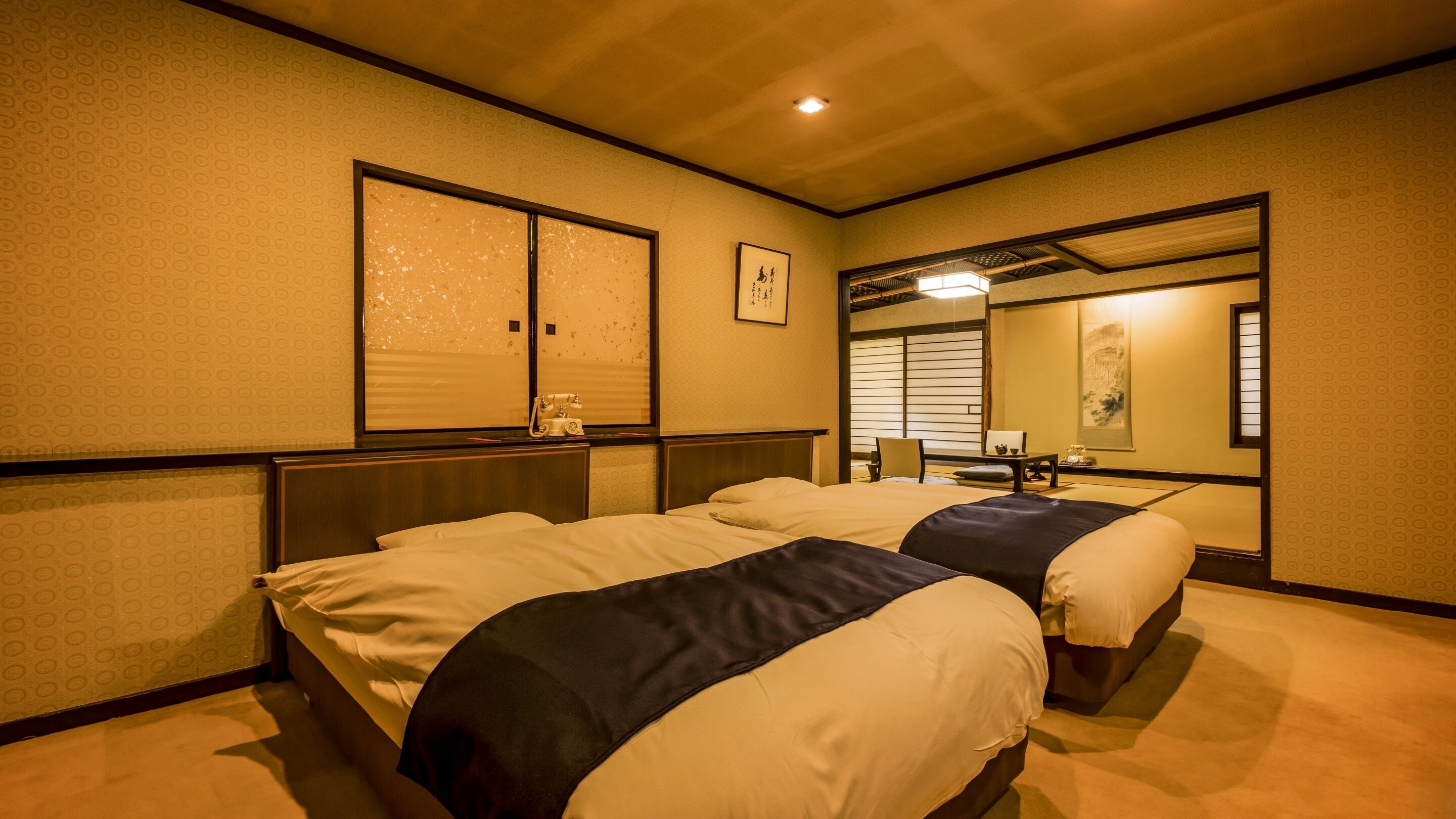 Una habitació d'hotel amb dos llits, un mirall gran i una porta corredissa tradicional japonesa.