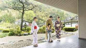 A traditional Japanese garden with a stone pathway, a wooden building, and a mountainous backdrop.