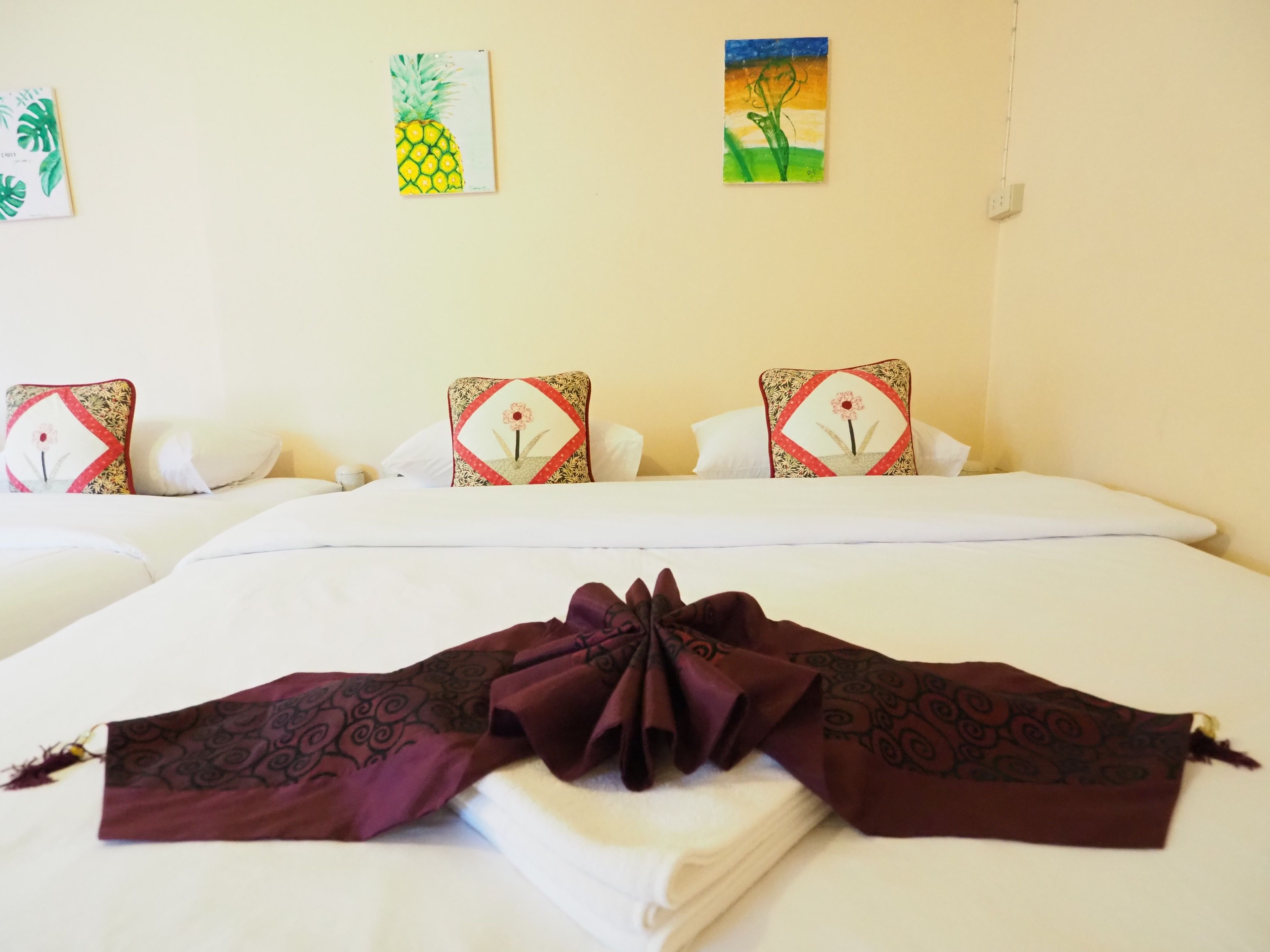 A hotel room with a neatly made bed, floral-patterned pillows, and wall art depicting tropical plants.