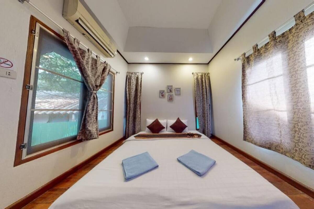 A hotel room with a bed, curtains, a window, and a wall-mounted air conditioner.