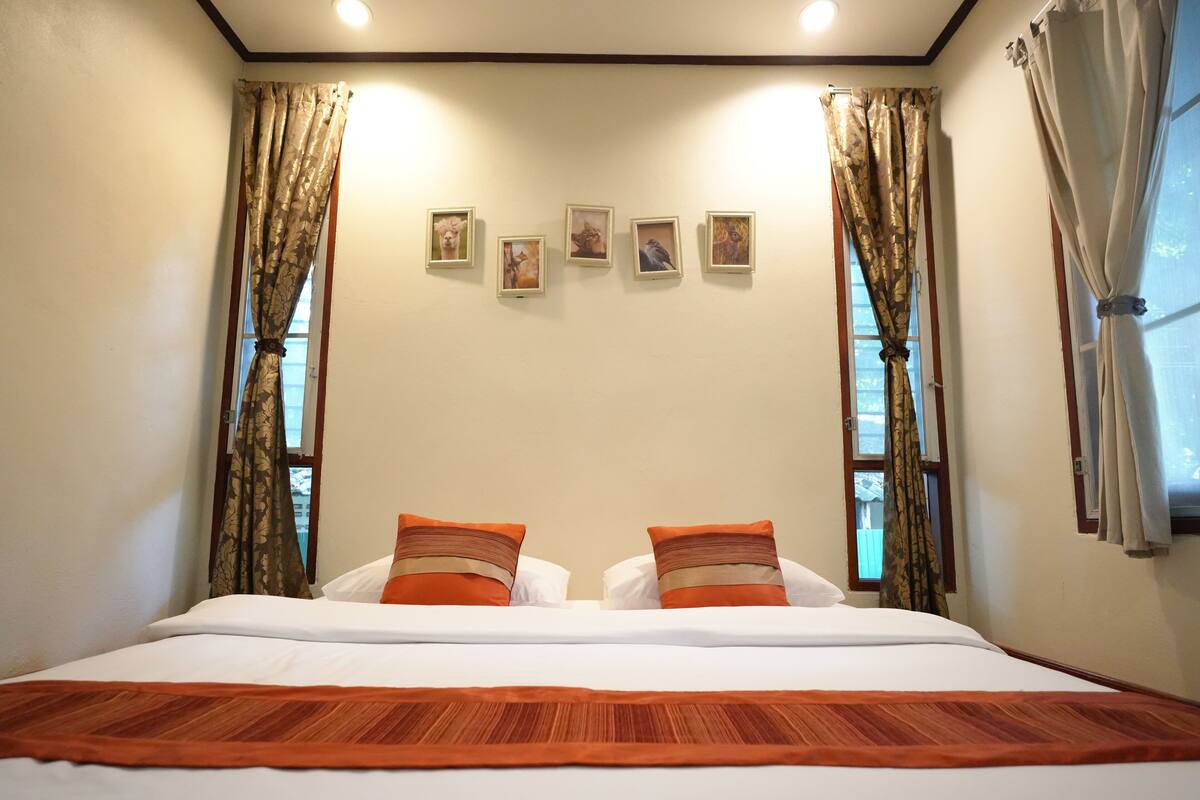 A room with a large bed, two pillows, a headboard, and a window with curtains.