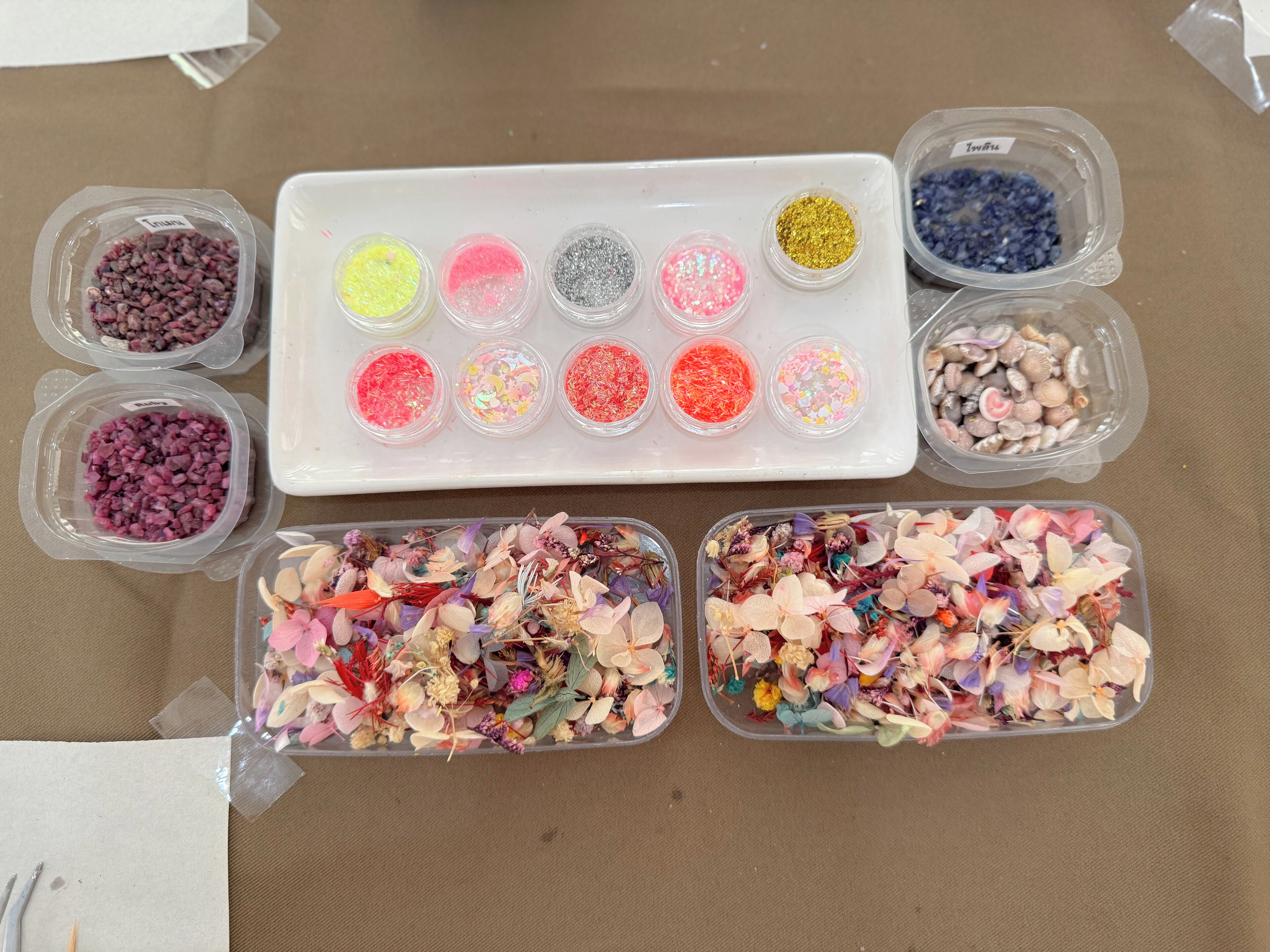 A variety of craft materials including beads, sequins, and dried flowers in clear containers.