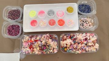 A variety of craft materials including beads, sequins, and dried flowers in clear containers.