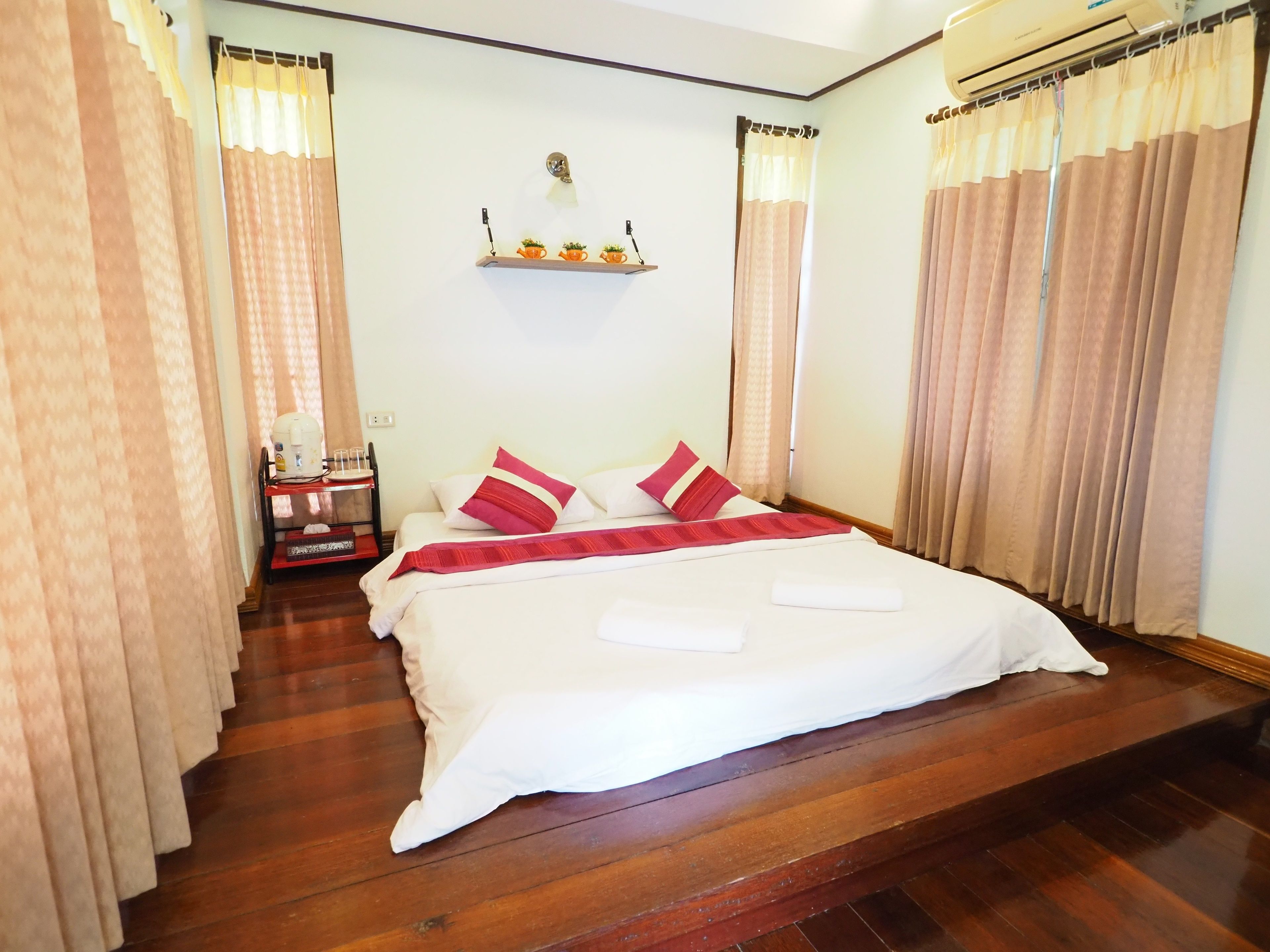 A neatly made bed with white and red bedding, a small bedside table with a lamp, and a shelf with decorative items.