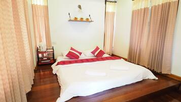 A neatly made bed with white and red bedding, a small bedside table with a lamp, and a shelf with decorative items.